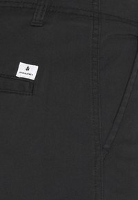 Schwarze Denim-Hosen mit einer glatten Textur, versehen mit einem weißen Etikett mit "JACK & JONES", das auf der hinteren Tasche genäht ist.