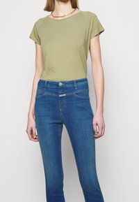 Camiseta de algodón verde oliva de manga corta y cuello redondo, combinada con vaqueros ajustados azules con diseño de cinco bolsillos.
