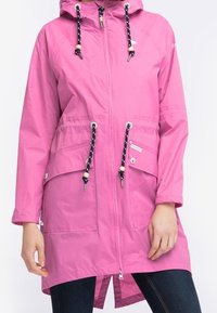 Vaaleanpunainen vedenpitävä takki, jossa on vetoketjukiinnitys, säädettävä huppu, kaksi etutaskua ja kontrastiväriset tummansiniset narut. Sileä, kevyt kangas.