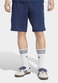 Ναυτικό μπλε αθλητικά σορτς από μαλακό ύφασμα, με ελαστική ζώνη. Συνδυασμένα με λευκές κάλτσες μέχρι το γόνατο με ναυτικές ρίγες και επώνυμα αθλητικά παπούτσια.