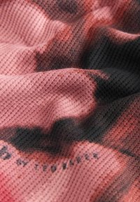 Textured fabric in pink and black hues, featuring a mesh weave pattern. Subtle fading and branding visible in lower corner.