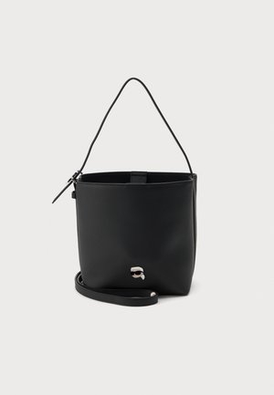 Sac seau en cuir noir avec une fine bandoulière et un petit logo argenté sur le devant, présenté sur un fond clair uni.