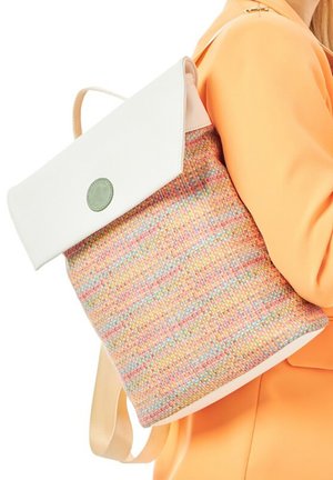 Woman wearing an orange jacket carries a multicolored woven backpack with a white flap and round green button.