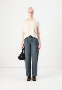 Beige túlméretezett póló, elhalványult kék, bő szabású farmernadrág, fekete mintás táska, és fekete bokacsizma. Minimalista design, laza illeszkedés.