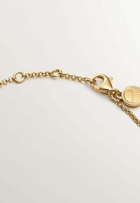 Cadena de oro con eslabones redondos, que presenta un cierre de langosta y una etiqueta circular. La textura suave y el acabado pulido realzan su diseño.