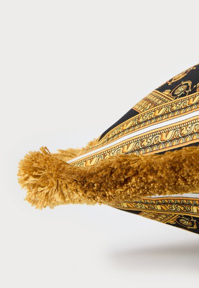 Κοντινό σε γωνία διακοσμητικού μαξιλαριού με ύφασμα σε χρυσό σχέδιο και παχύ, χρυσοκαφέ υφασμάτινο κρόσσι.