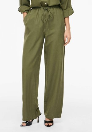 Široké nohavice olivovo zelenej farby s pásom na šnúrku, nosené s vyhrnutými rukávmi a čiernymi sandálmi na vysokom podpätku s otvorenou špičkou.