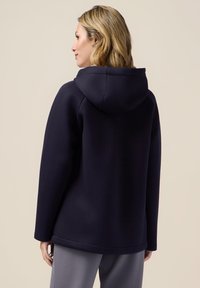 Felpa cappuccio navy con vestibilità rilassata, caratterizzata da una superficie tessile liscia e un design minimalista, mostrata da un angolo laterale.
