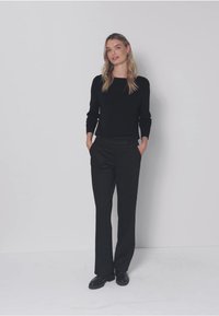 Zwarte top met lange mouwen gecombineerd met op maat gemaakte zwarte broek. De outfit heeft een losse pasvorm, met zakken en een gladde textuur. Eenvoudig ontwerp.