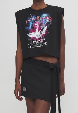 Black cropped sleeveless top with swan, lightning graphics, and "COUTURE" text paired with a black wrap skirt tied at the waist.
