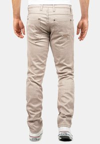 Pantalons en velours côtelé beige avec des rayures verticales, dotés de poches arrière et de quincaillerie métallique, associés à des baskets blanches.