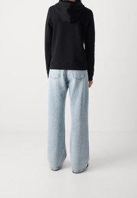 Sudadera negra con capucha y vaqueros de pierna ancha azul claro. Los vaqueros tienen una textura desgastada con bolsillos traseros visibles y dobladillos sin rematar.