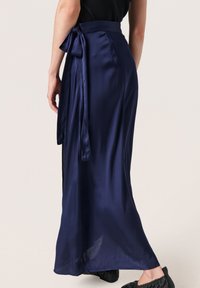 La skirt wrap satin marin cu un fundiță legată în talie și un design elegant, fluid. Țesătura are o textură netedă și un luciu subtil.