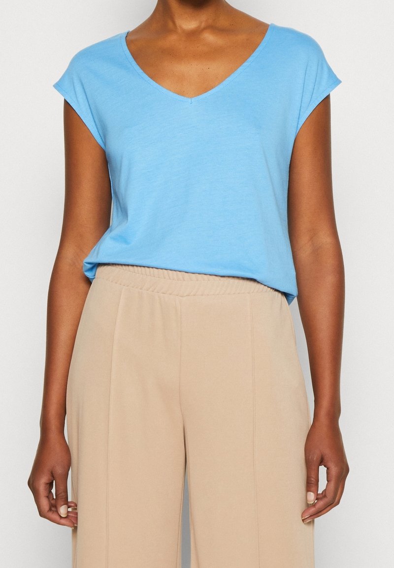 Světle modré tričko s krátkým rukávem a véčkovým výstřihem vyrobené z měkké látky, spojené s béžovými kalhotami s elastickým pasem. Jednoduchý design, uvolněný střih.