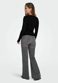 Zwart geribbeld langemouwen top gecombineerd met grijze flare jeans. De jeans hebben een middelhoge taille en achterzakken met subtiele stikdetails.