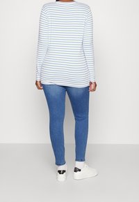 Top de manga larga blanco con rayas azul claro, combinado con jeans ajustados azules y zapatillas blancas con un acento negro en el talón.