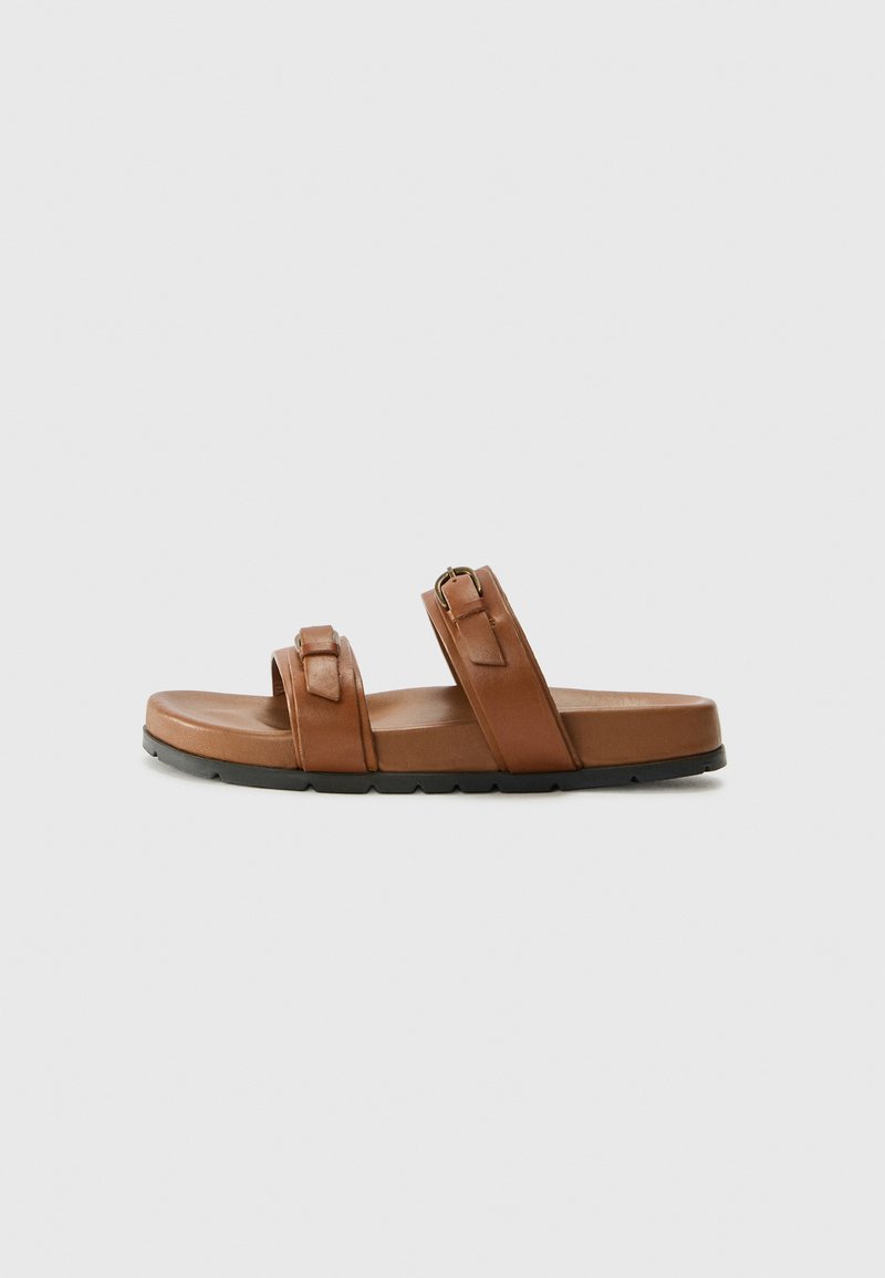 Brune lær slidesandal med to justerbare stropper og en teksturert fotbredde. Svart gummisåle, flat design med minimal heving.