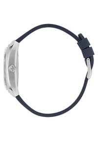 Montre en acier inoxydable argenté avec un cadran clair, un bracelet en silicone bleu marine et une boucle en métal. Elle présente un boîtier rond et un logo distinctif sur le côté.