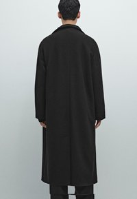 Cappotto nero con trama uniforme, lunghezza lunga, colletto ampio e vestibilità ampia. La parte posteriore presenta un design pulito senza elementi metallici visibili.