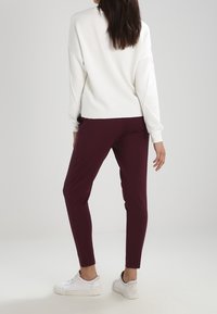 Bílá mikina, maroon slim-fit kalhoty a bílé tenisky. Tkanina vypadá měkce; mikina má spadlé ramena a uvolněný střih.