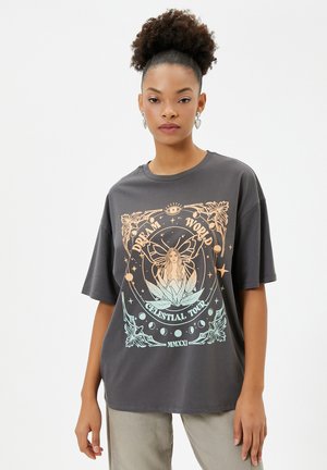 Camiseta gráfica de tejido gris oscuro con un diseño celestial colorido que presenta una figura central, estrellas y el texto "TOUR CELESTE DEL MUNDO DE LOS SUEÑOS".