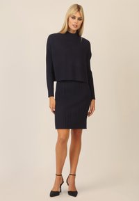 Navy-blaues, geripptes Strick-Zweiteiler-Kleid mit einem verkürzten Oberteil und langen Ärmeln sowie einem figurbetonten Rock. Schlichte Silhouette mit strukturiertem Stoff.