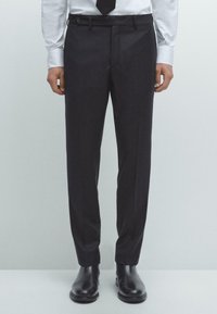 Donkergrijze op maat gemaakte broek met een gladde textuur, platte voorkant en een riemlus. Gecombineerd met zwarte leren schoenen.