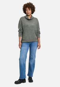 Grauer Strickpulli mit einem Schalkragen, kombiniert mit blauen geraden Jeans und schwarzen Plateau-Stiefeln. Der Pullover hat eine rippenartige Textur.