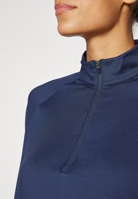 Tumesinine pool-krae sportlik pullover, valmistatud venivast kangast, millel on kõrge krae ja lamedad õmblused sujuvaks sobivuseks.