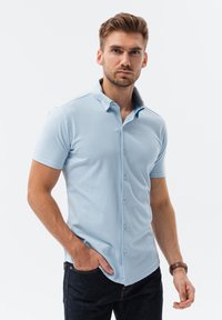 Camisa polo de manga corta azul claro con cuello abotonado, hecha de una tela texturizada, con un corte ajustado y detalles de diseño sutiles.