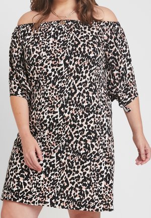 Vrouw die een korte off-shoulder jurk draagt met een zwart-wit-roze luipaardprint en driekwart mouwen die aan de uiteinden zijn gestrikt.