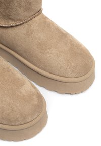 Beżowe zamszowe botki za kostkę z teksturowaną cholewką, okrągłym noskiem i płaską gumową podeszwą z ryflowanym wzorem dla lepszej przyczepności.