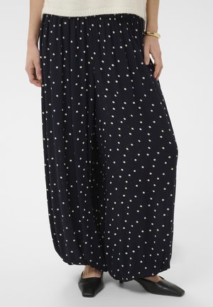 Marineblaue, weit geschnittene Hosen mit weißen Polka-Dots, elastischem Bund, kombiniert mit schwarzen spitzen Ballerinas und einem goldenen Armband am linken Handgelenk.