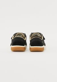 Scarpe in suede nere con accenti beige, cinturini in velcro e una suola intermedia bianca. La suola in gomma presenta un motivo testurizzato color gomma.