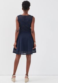 Robe bleu marine avec un corsage ajusté, des détails en dentelle en haut et à l'ourlet, une jupe évasée et une texture lisse.