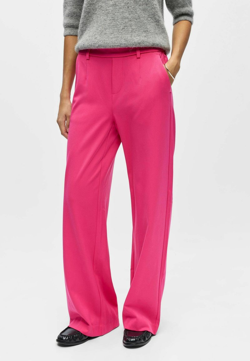 Pantalon large fuchsia à la texture lisse, doté de poches latérales et d'une taille légèrement haute ; porté avec des chaussures plates noires.