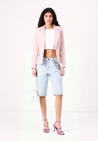 Světle růžový přiléhavý blejzr přes bílý crop top, doplněný světle modrými džínovými bermudami. Doplňky zahrnují bílou tašku a fialové podpatky.