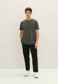Gray short-sleeve t-shirt made of soft fabric, paired with black trousers. The outfit is completed with white sneakers. Plain design, no patterns.