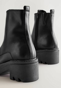 Black leather ankle boots with a chunky sole, featuring a side zipper, a smooth texture, and reinforced stitching along the seams.