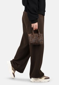 Mini borsa a tracolla con motivo leopardato, realizzata in pelle sintetica, dotata di manici piccoli e cuciture a vista, tenuta da una persona in abbigliamento casual.