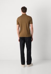 Polo de culoare maro, cu mâneci scurte, design potrivit, textură netedă, asortat cu pantaloni negri și adidași deschiși, prezentat din spate.
