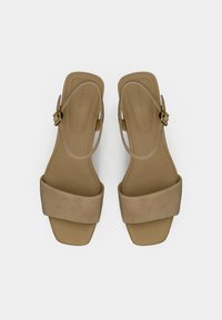 Μπεζ σανδάλια με λουράκι πίσω, με φαρδύ, μαλακό σουέντ λουράκι και κομψό τακούνι. Διαθέτουν χρυσή πόρπη για ρυθμιζόμενο κάλλυμα και λεία εσωτερική επένδυση.