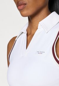 Polo alb fără mâneci cu guler, având accente vișinii pe margini și un eticheta cu logo-ul "Ted Baker Sport".