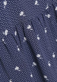 Tessuto blu navy con pois bianchi e piccoli motivi floreali. Presenta un design plissettato, una texture liscia e un materiale leggero.