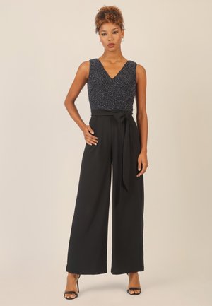 Schwarzer Jumpsuit mit weitem Bein und tiefem V-Ausschnitt sowie einem glitzernden marineblauen Oberteil. Verfügt über eine gebundene Taille für eine verstellbare Passform und eine glatte Textur.