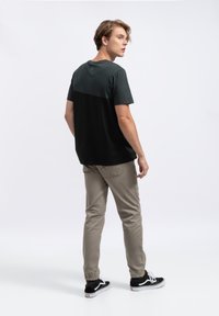 T-shirt a maniche corte con una parte inferiore nera e una parte superiore verde scuro, abbinato a pantaloni beige chiaro e sneakers nere.