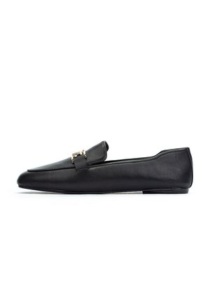 Mocasín de cuero negro con diseño de punta afilada, que presenta una hebilla de acento dorado en la parte delantera y una suela fina y plana.