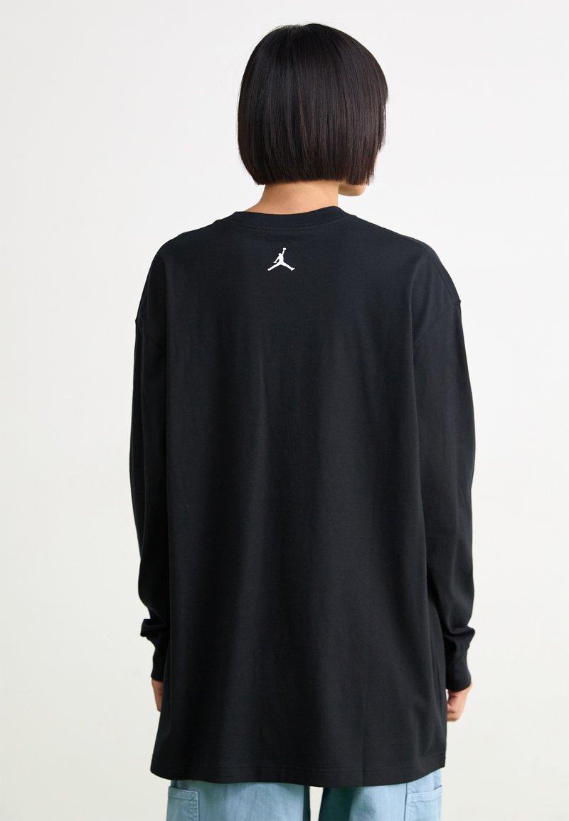 Camisa negra de manga larga con un corte holgado, que presenta un logo Jumpman blanco en la parte superior de la espalda. Fabricada en algodón suave con una textura lisa.
