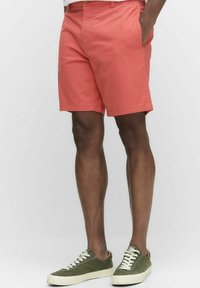 Korallfärgade shorts med rak framsida och sidofickor, tillverkade av lättviktsmaterial. Kombinerade med olivgröna sneakers med vita snören.