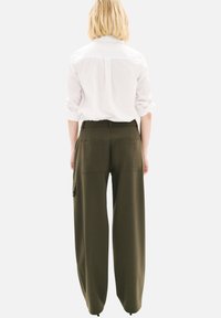 Chemise blanche à manches longues associée à un pantalon large olive avec deux poches arrière et une poche cargo sur le côté. Texture de tissu lisse.